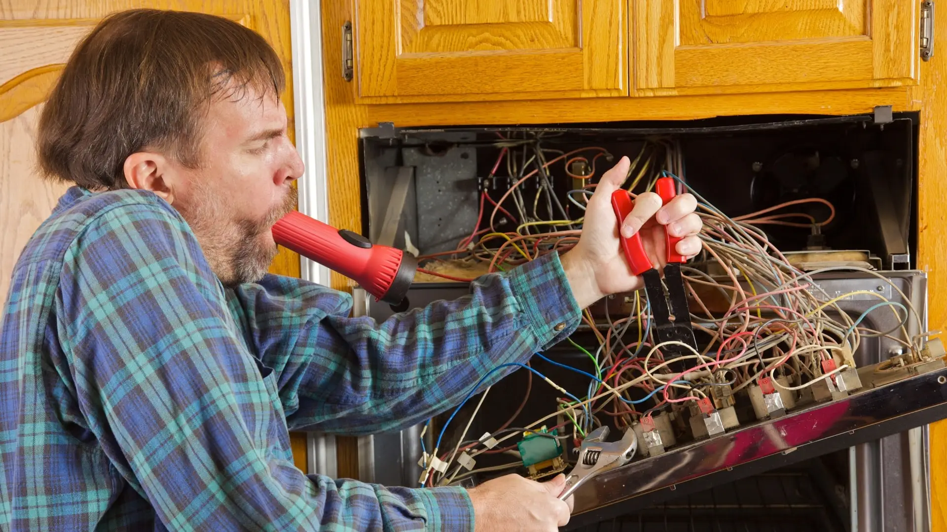 Confused man trying to work out and fix the inner mechanisms of an oven at home.